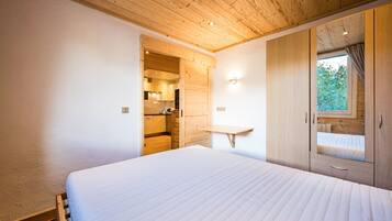 A bedroom with a wooden ceiling, a bed, a wardrobe, and a window.