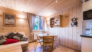Ein Holzblockhaus-Interieur mit Esstisch, Stühlen, einer Couch, einer Küchenzeile und einem Poster an der Wand.