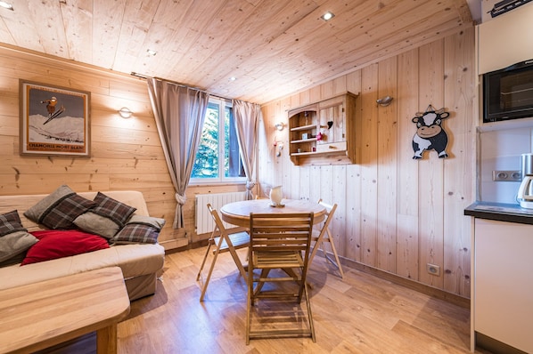 L’intérieur d’une cabane en bois comprend une table à manger, des chaises, un canapé, un coin cuisine et une affiche accrochée au mur.