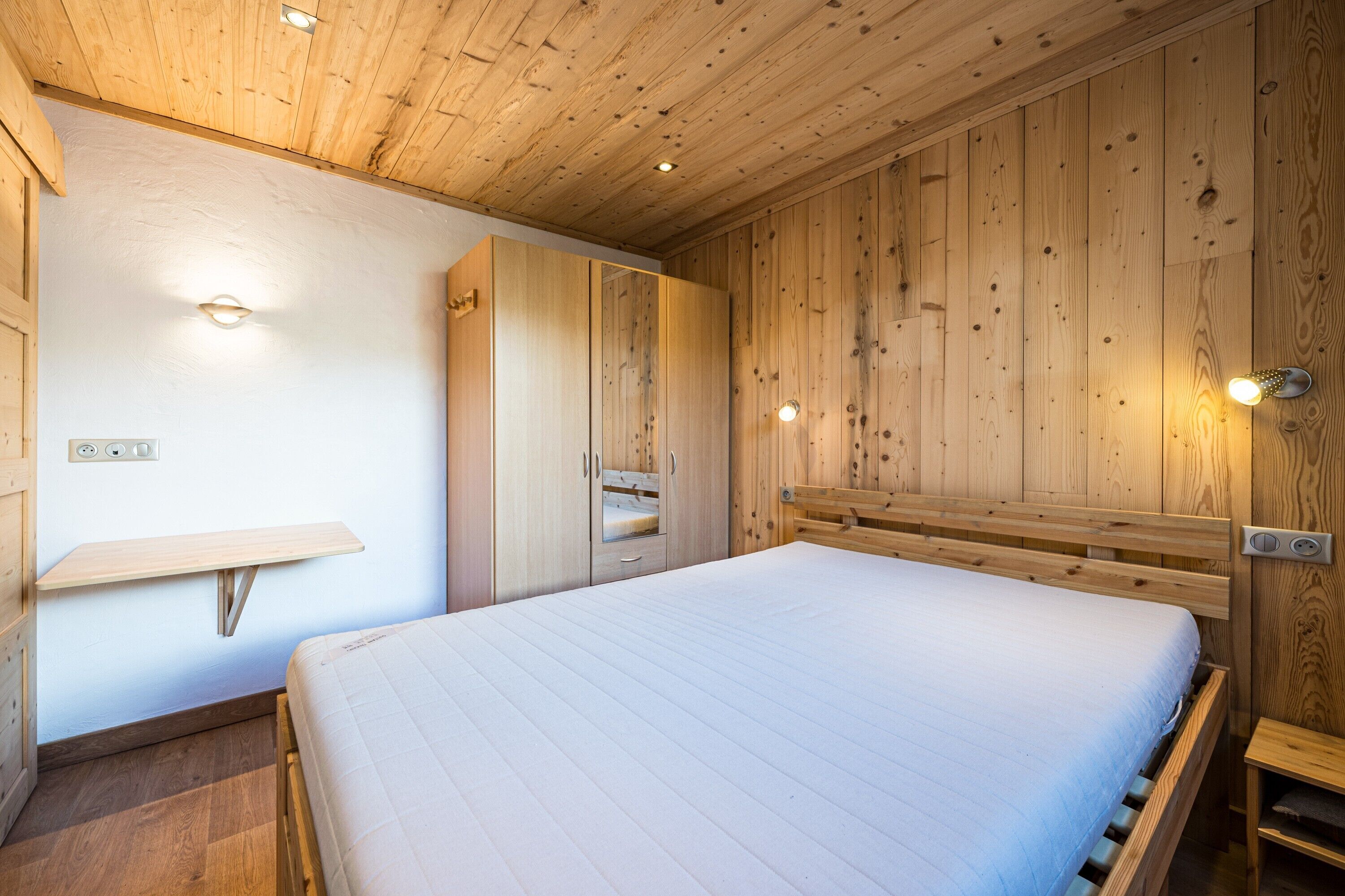Een slaapkamer met een houten plafond, een bed, een houten kledingkast en een nachtkastje.