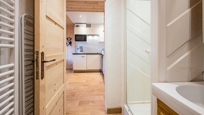 Ein schmaler Flur führt zu einer Küche mit Holzboden, einer Mikrowelle und Schränken.