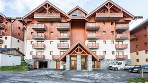 A multi-story hotel with wooden balconies, a stone entrance, and a parking area. - Apartment 'Vacation Rental' with Mountain View and Balcony (Saint François Longchamp)