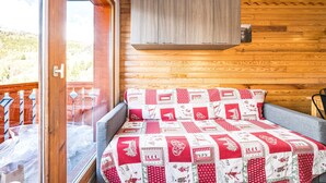 A wooden cabin room with a bed, a window, and a view of the outdoors. - Apartment 'Vacation Rental' with Mountain View and Balcony (Saint François Longchamp)