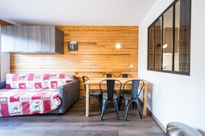 Una stanza con parete in legno, un tavolo da pranzo con sedie, un divano con coperta fantasia e una finestra.