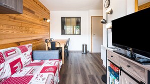 A compact room with a sofa, a dining table, a TV, and a small trash bin. - Apartment 'Vacation Rental' with Mountain View and Balcony (Saint François Longchamp)