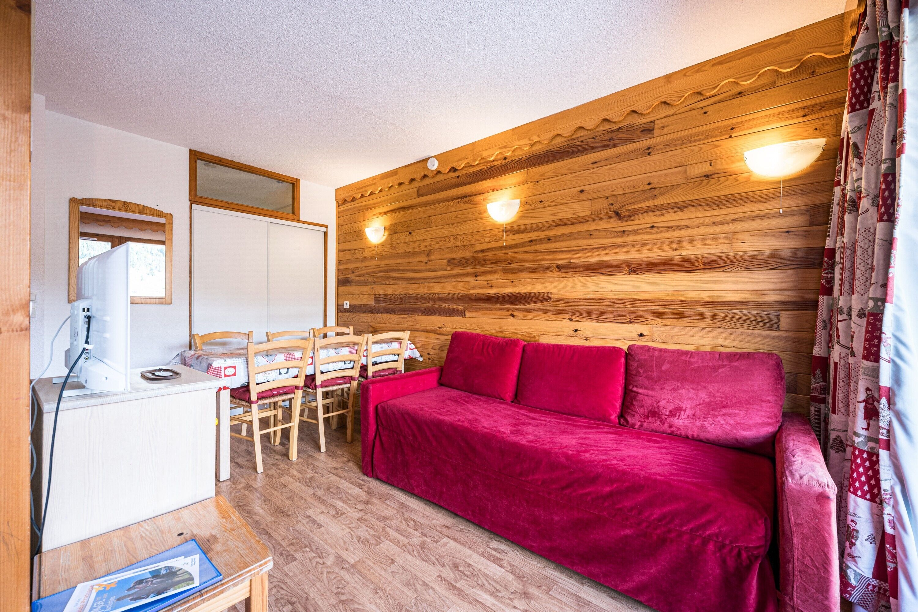 Ein Zimmer mit einer Holzwand, einem roten Sofa, einem Holztisch mit Stühlen und einem weißen Schrank.