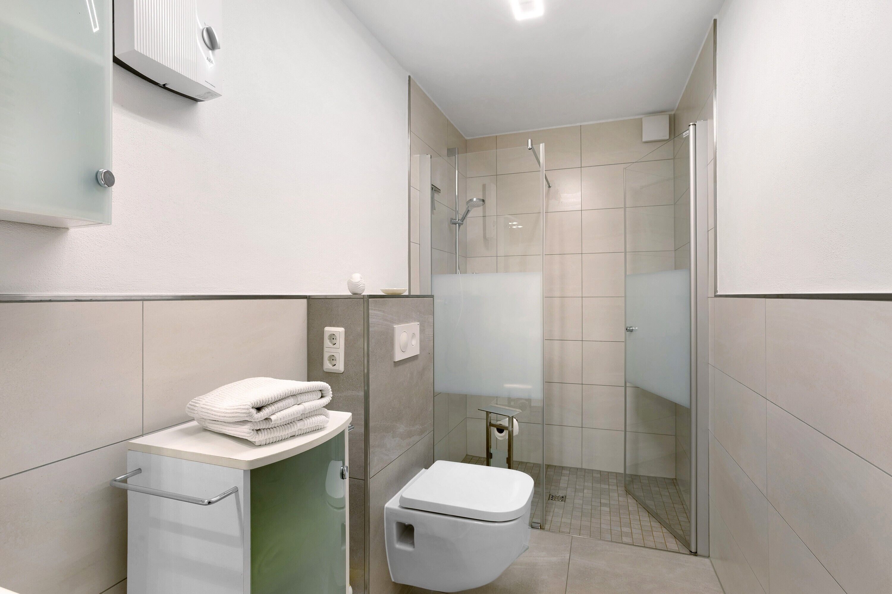 Et moderne badeværelse med toilet, glasbrusekabine og håndklædestang.
