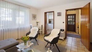 A living room with a sofa, two chairs, a glass coffee table, a vase with flowers, and a view of the kitchen through a doorway. - 'Bilstein' Apartment in a Quiet, Central Location (Lennestadt)