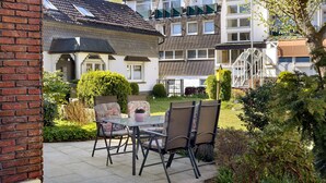 A patio with a glass table and chairs, surrounded by a brick wall and greenery. - 'Bilstein' Apartment in a Quiet, Central Location (Lennestadt)