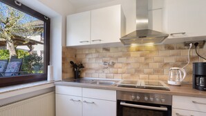 A modern kitchen with white cabinets, a stainless steel range hood, a built-in oven, and a window with a view of the outdoors. - 'Bilstein' Apartment in a Quiet, Central Location (Lennestadt)