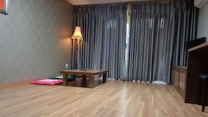 A room with a wooden floor, a table, a lamp, a pink cushion, and a TV. - Residence Hotel Lamia (Daejeon)