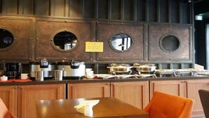 A kitchen area with a central island, wooden cabinets, and a seating area with orange chairs. - Residence Hotel Lamia (Daejeon)