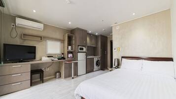 Habitación de hotel con cama, escritorio con computadora, televisión, microondas y kitchenette pequeño.
