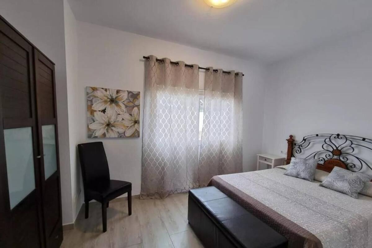 Une chambre à coucher comprenant un lit, une chaise, un banc, une table de chevet, une lampe et un tableau accroché au mur.