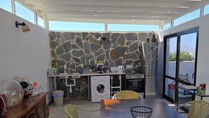 A modern kitchen with stone backsplash, a washing machine, and a dining area with wicker chairs and a wooden table. - Paradise Homes Lanzarote (Nazaret)