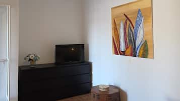 A room with a ceiling fan, a flat-screen TV on a black dresser, a painting on the wall, and a woven rug on the floor.