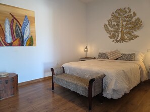 A bedroom with a bed, a bench, a nightstand, a lamp, and a wall art piece. - Paradise Homes Lanzarote (Nazaret)
