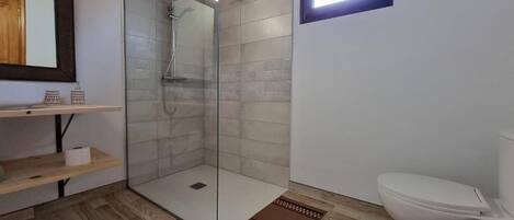A modern bathroom with a glass-enclosed shower, a toilet, and a wooden shelf with toiletries.