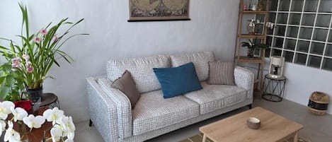 A living room with a patterned sofa, a coffee table, a world map on the wall, and a window with a grid pattern.