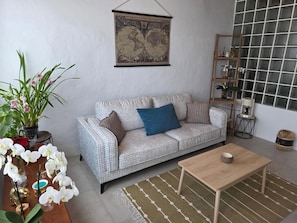 A living room with a patterned sofa, a coffee table, a world map on the wall, and a window with a grid pattern.