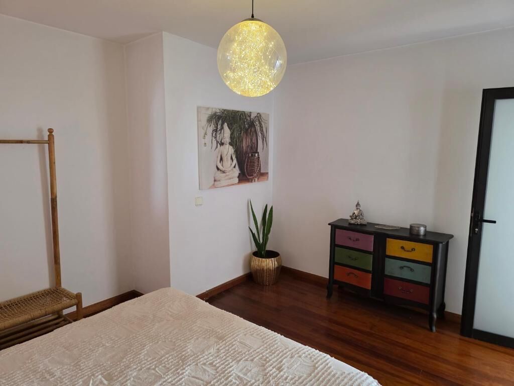 A bedroom with a bed, a bedside table, a wall-mounted lamp, a potted plant, and a colorful dresser.