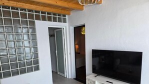 A modern living room with a large flat-screen TV on a white console, a wooden ceiling, and a large window with frosted glass panels. - Paradise Homes Lanzarote (Nazaret)