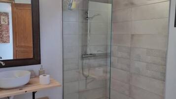Un baño moderno con ducha envuelta en vidrio, un lavabo blanco y un estante de madera.