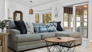 Ein modernes Wohnzimmer mit einem grauen Sofa, einem Holztisch und einer hängenden Pendelleuchte.