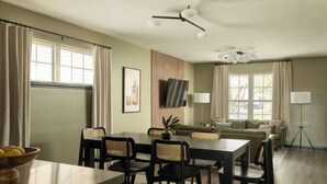 A dining area with a table and chairs, a sofa, and a television mounted on the wall.