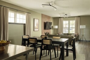A dining area with a table and chairs, a sofa, and a television mounted on the wall.