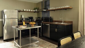 A modern kitchen with a stainless steel refrigerator, a coffee machine, a sink, and a dining area with a table and chairs.