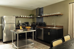 A modern kitchen with a stainless steel refrigerator, a coffee machine, a sink, and a dining area with a table and chairs.
