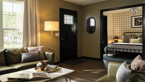 A well-lit room with a sofa, a table with a book and a vase, a lamp, a bed with a headboard, and a door with a window.