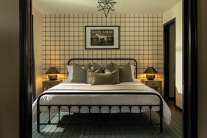 A neatly made bed with a headboard, flanked by two bedside tables with lamps, in a room with a plaid wallpaper and a framed picture on the wall.