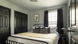 A bedroom with a bed, a nightstand, a lamp, a window with curtains, and a door.