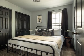 A bedroom with a bed, a nightstand, a lamp, a window with curtains, and a door.