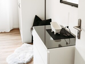 Une salle de bain blanche avec une douche à parois de verre, une baignoire blanche posée sur un tapis noir et un tapis blanc et moelleux sur le sol.