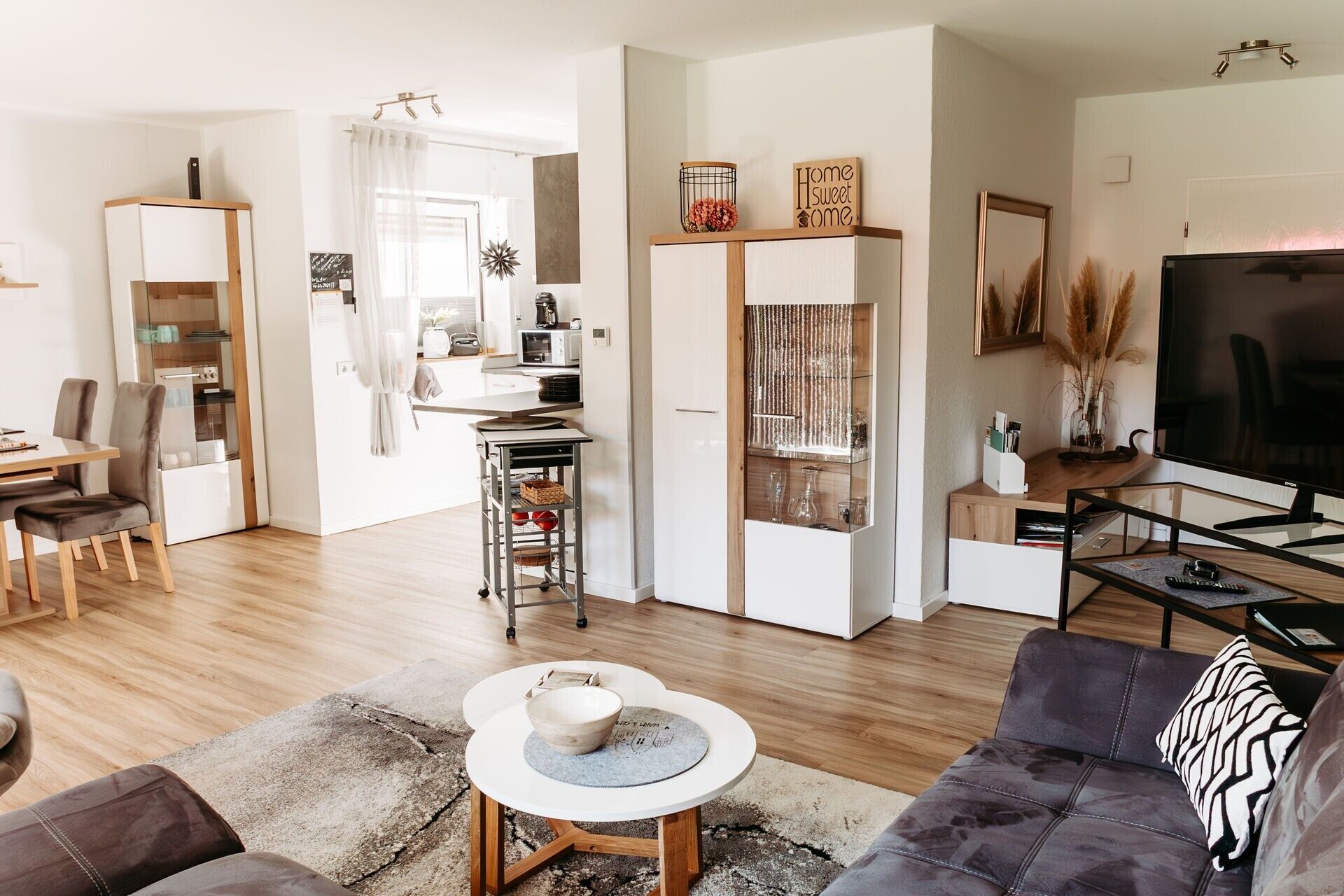 A modern living room with a sofa, a coffee table, a TV, and a kitchen area with a microwave.