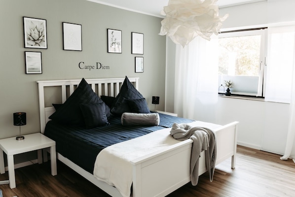 Un dormitorio con cama, mesitas de noche, una ventana y decoración en la pared.