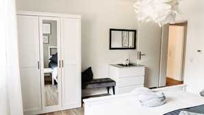 Ein Schlafzimmer mit Bett, Nachttisch, Kleiderschrank, Spiegel und kleinem Schreibtisch mit Lampe.