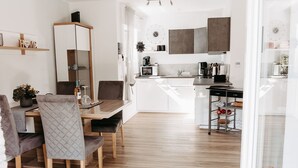 Eine moderne Küche mit weißen Schränken, einem Essbereich mit Holztisch und -stühlen sowie einer Kücheninsel mit Spüle.