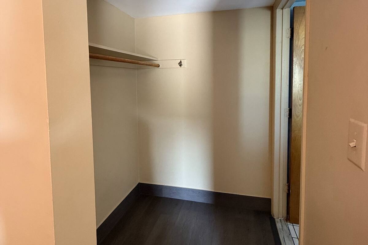 Un pasillo estrecho con una viga de madera a la izquierda, un interruptor de luz a la derecha y una puerta al final.