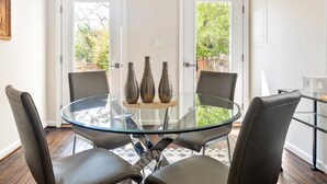 Un coin repas avec une table en verre entourée de quatre chaises, deux portes donnant sur l’extérieur et trois vases décoratifs posés sur la table.