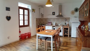 Una cocina con una mesa y sillas de madera, una estufa y un lavamanos. Hay botes de basura rojos y un extintor en el suelo.