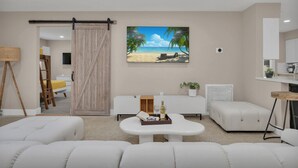 Un salon moderne avec une porte coulissante de style grange, un grand tableau sur le thème de la plage, un canapé blanc, une petite table avec un plateau, et un coin cuisine à l’arrière-plan.