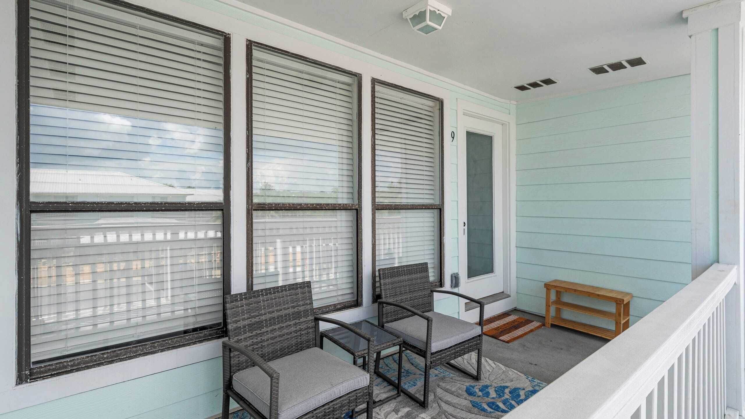 A porch with three wicker chairs and a small table, a wooden bench, and a door with a number '9' on it.