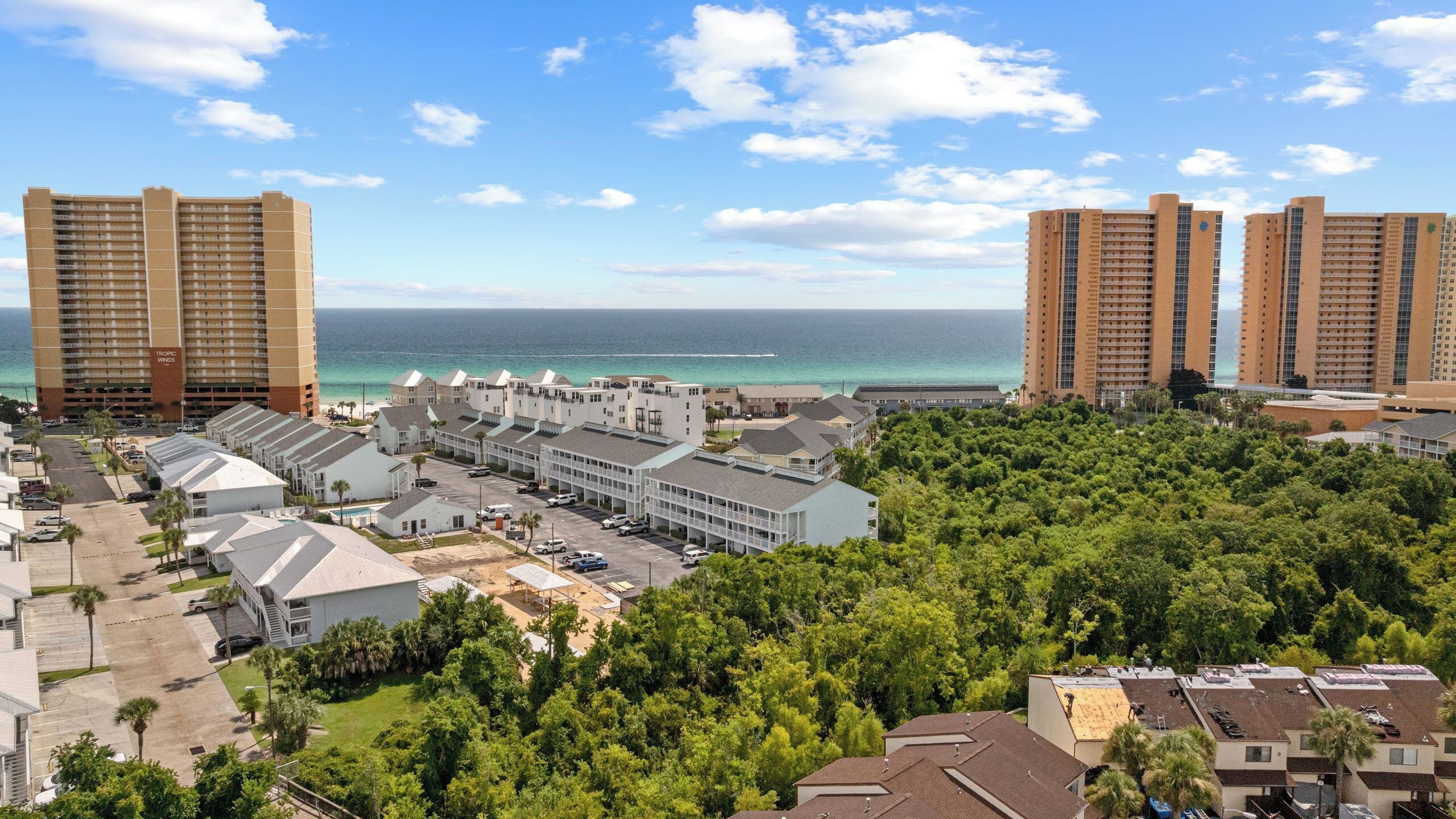 A coastal hotel area with multiple high-rise buildings, a parking lot, and lush greenery.