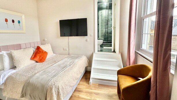 A hotel room with a bed, a TV, a shower, and a chair.