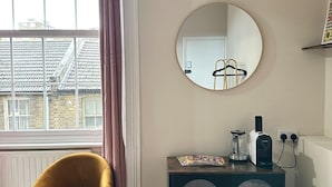 A room with a window, a round mirror, a small cabinet, and a mustard-colored chair.