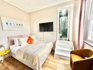 A bedroom with a bed, a TV mounted on the wall, a chair, and a staircase leading to a bathroom. - Chic studio flat in Camden (Greater London)